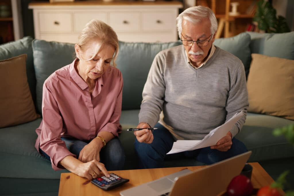 Senior couple reviews financial documents on the sofa during the daytime, working on insurance matters