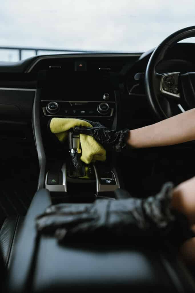 Nettoyage intérieur voiture : levier vitesse Main gantée de noir nettoyant le levier de vitesse de voiture avec une microfibre jaune près du bouton ECON.
